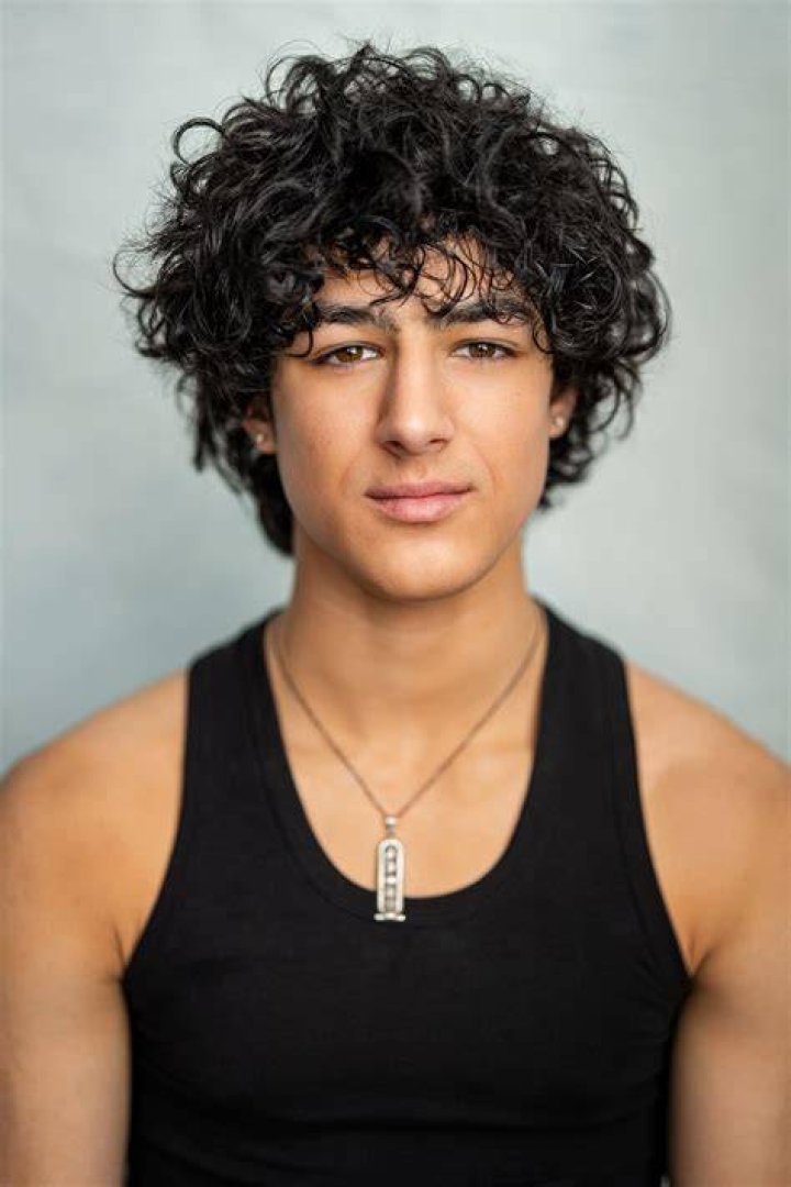 Bodhi Sabongui is standing on the ledge of a building showing his biceps.