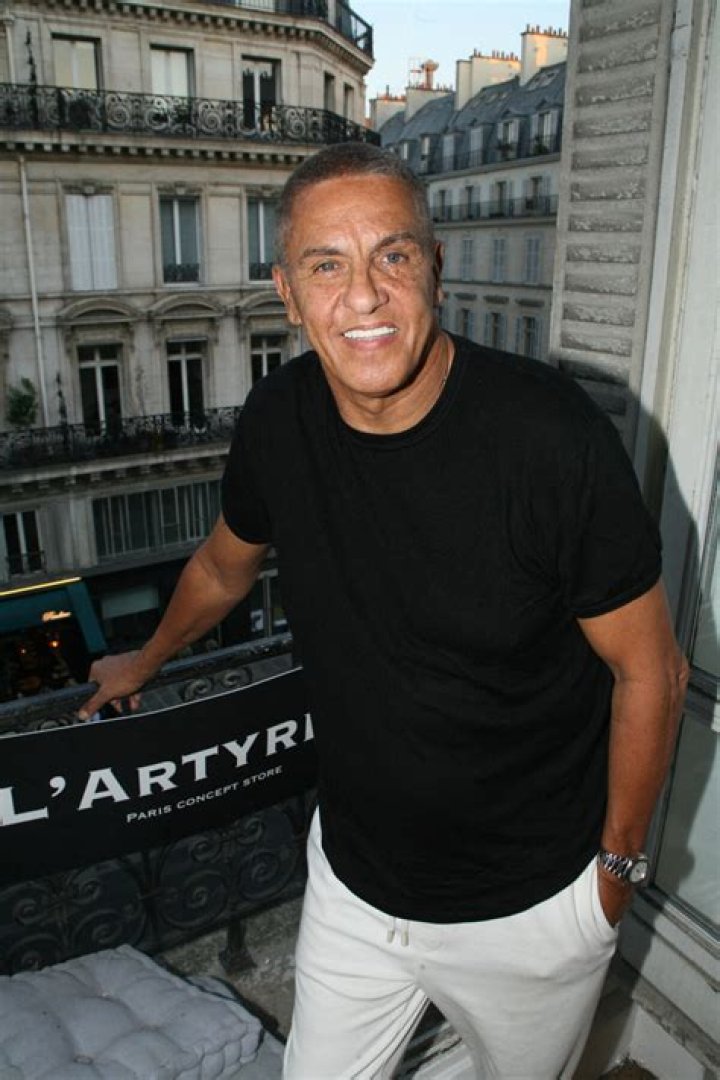 Samy Naceri is wearing a blue coat and pant with black shirt posing for Instagram post.